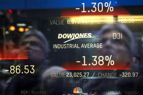Numbers for the Dow Jones Industrial Average are displayed on a screen, with a person's reflection.