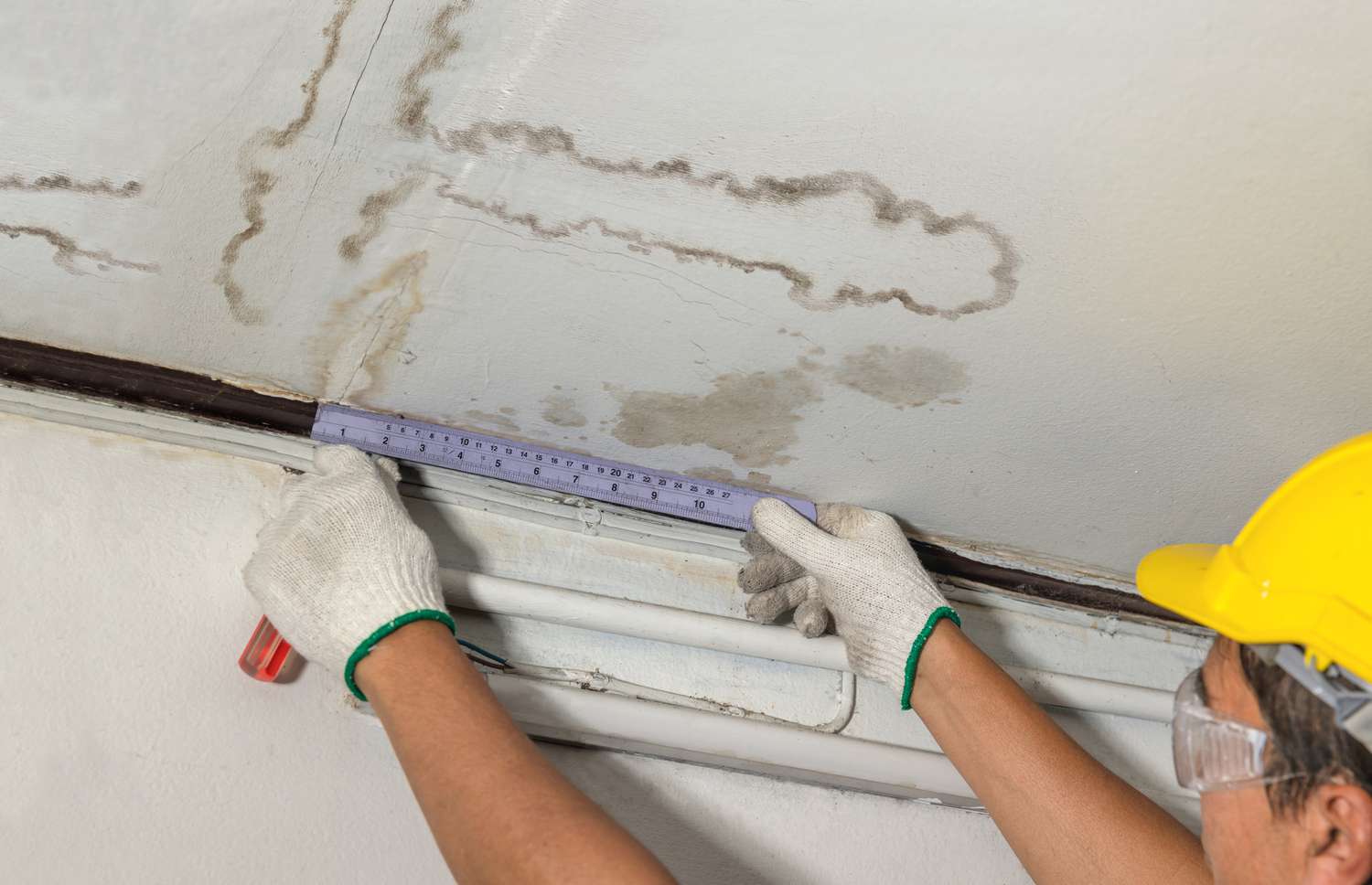 Worker fixing pipe in water-stained ceiling