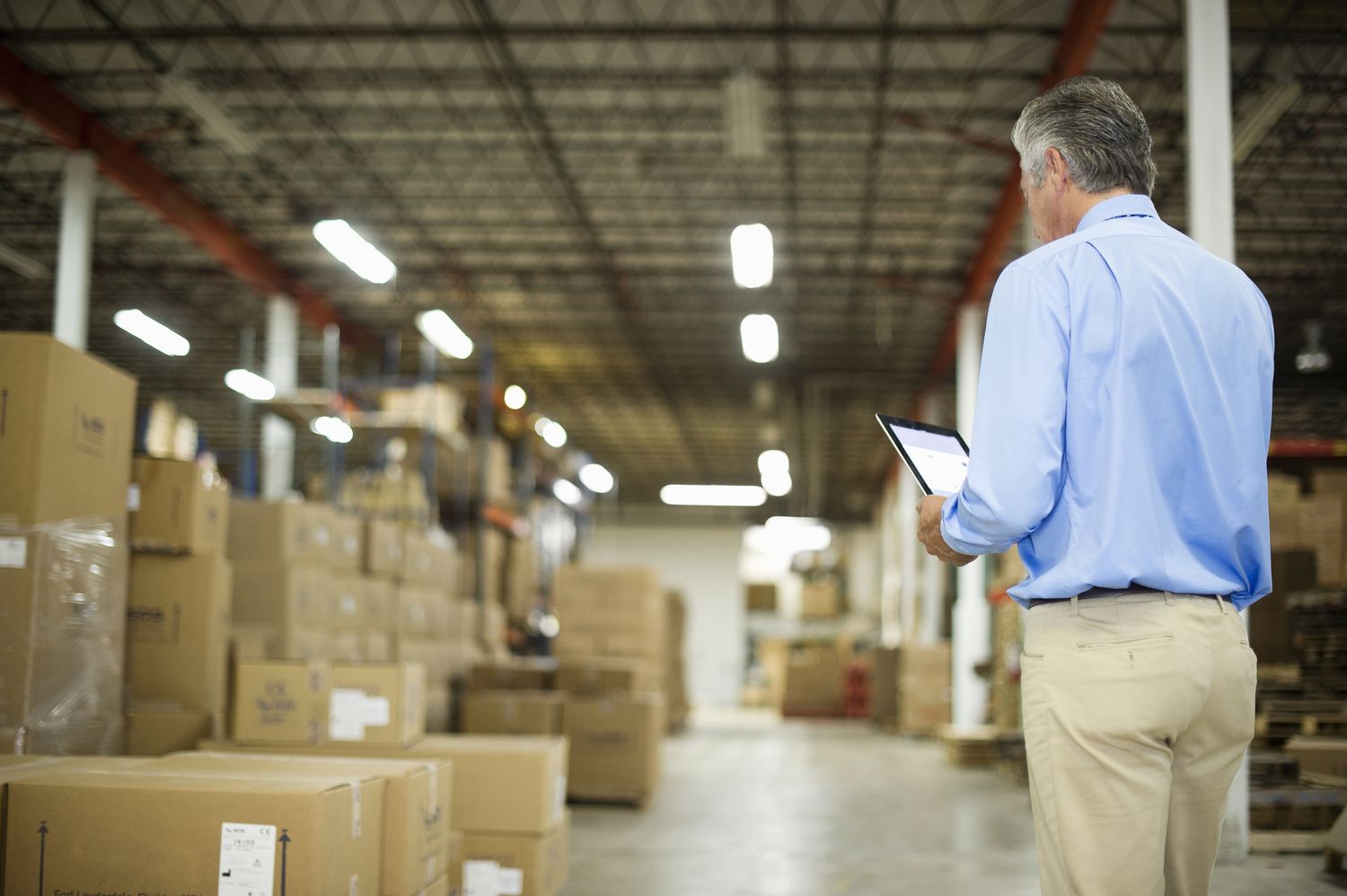 well dressed man standing in a warehouse with boxes looking at a tablet