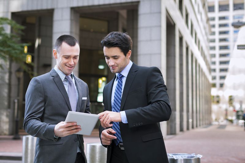 Two stockbrokers look at an amended proxy statement for a company they follow on a pad computer.