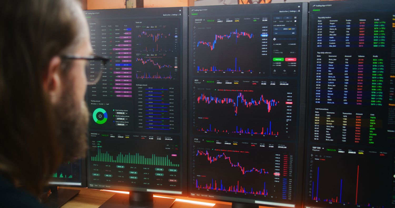 A trader sitting in front of several computer screens showing candlestick charts and other data.
