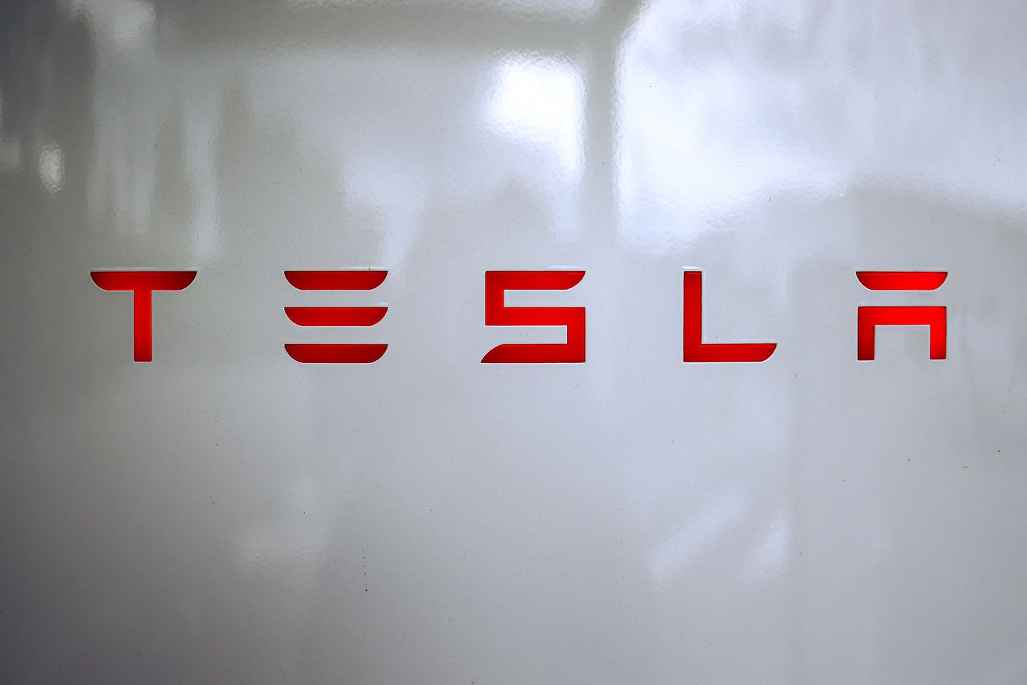 The red Tesla logo is seen on a white charging station.
