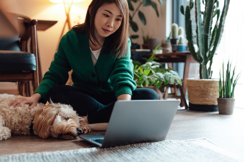 Young person with her dog while working on a laptop.