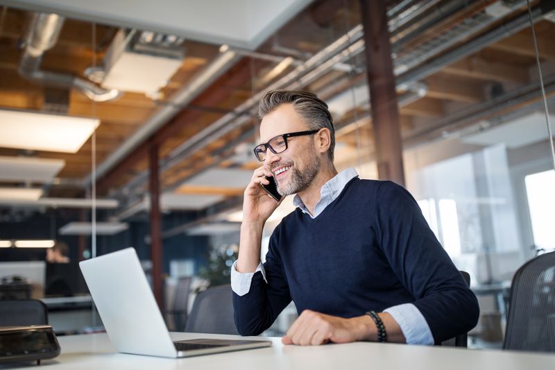 Professional in a modern office on his phone while looking at his laptop