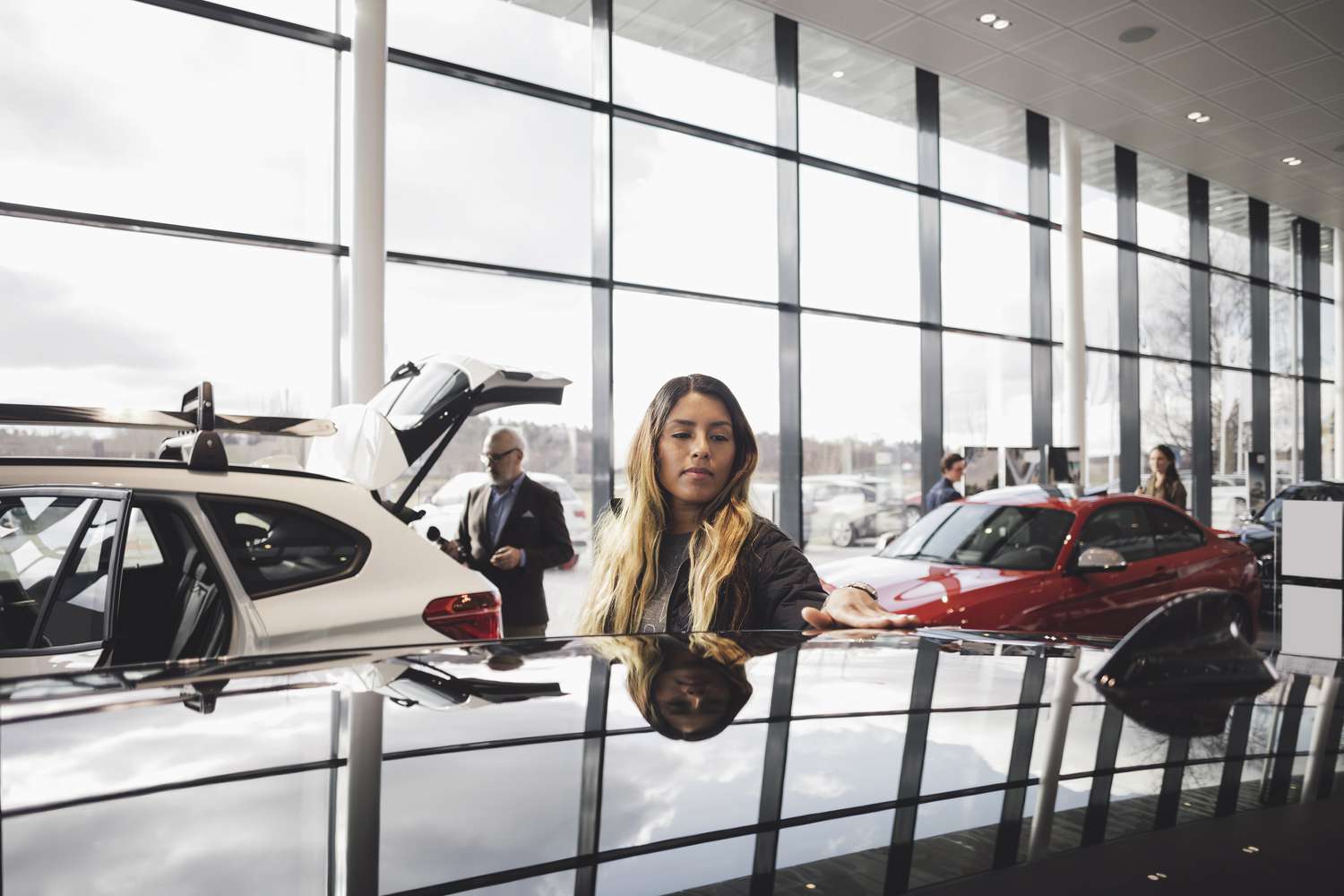 A wealthy shopper runs a hand over the top of a new car sitting in a dealership showroom. 