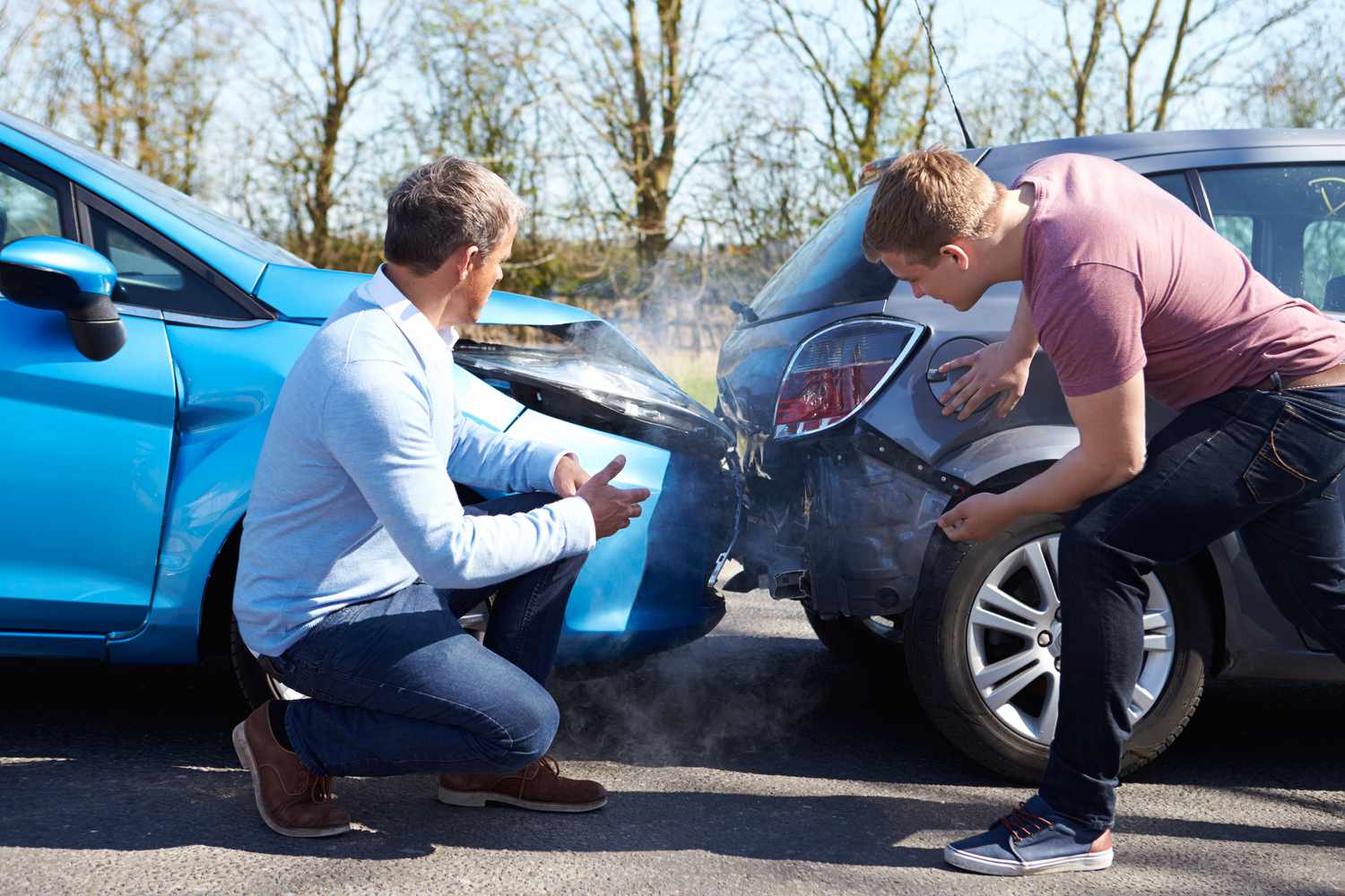 Two men look at their damaged cars after an accident