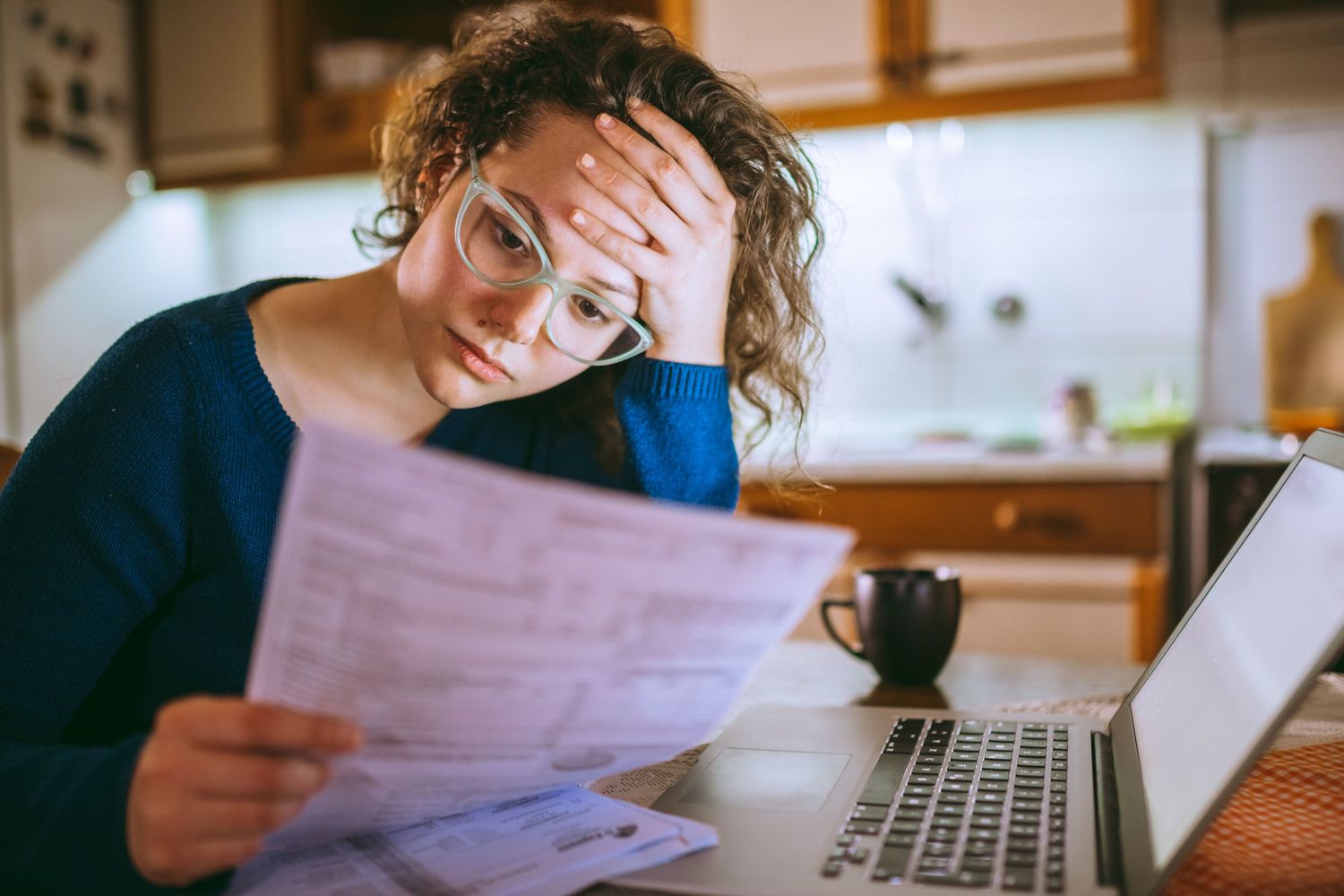 Individual reviewing bills at home in kitchen with a worried look