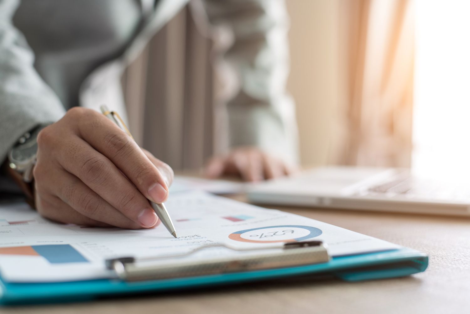 a person from the chest down writing on a clipboard with a pen. the clipboard shows graphs and charts