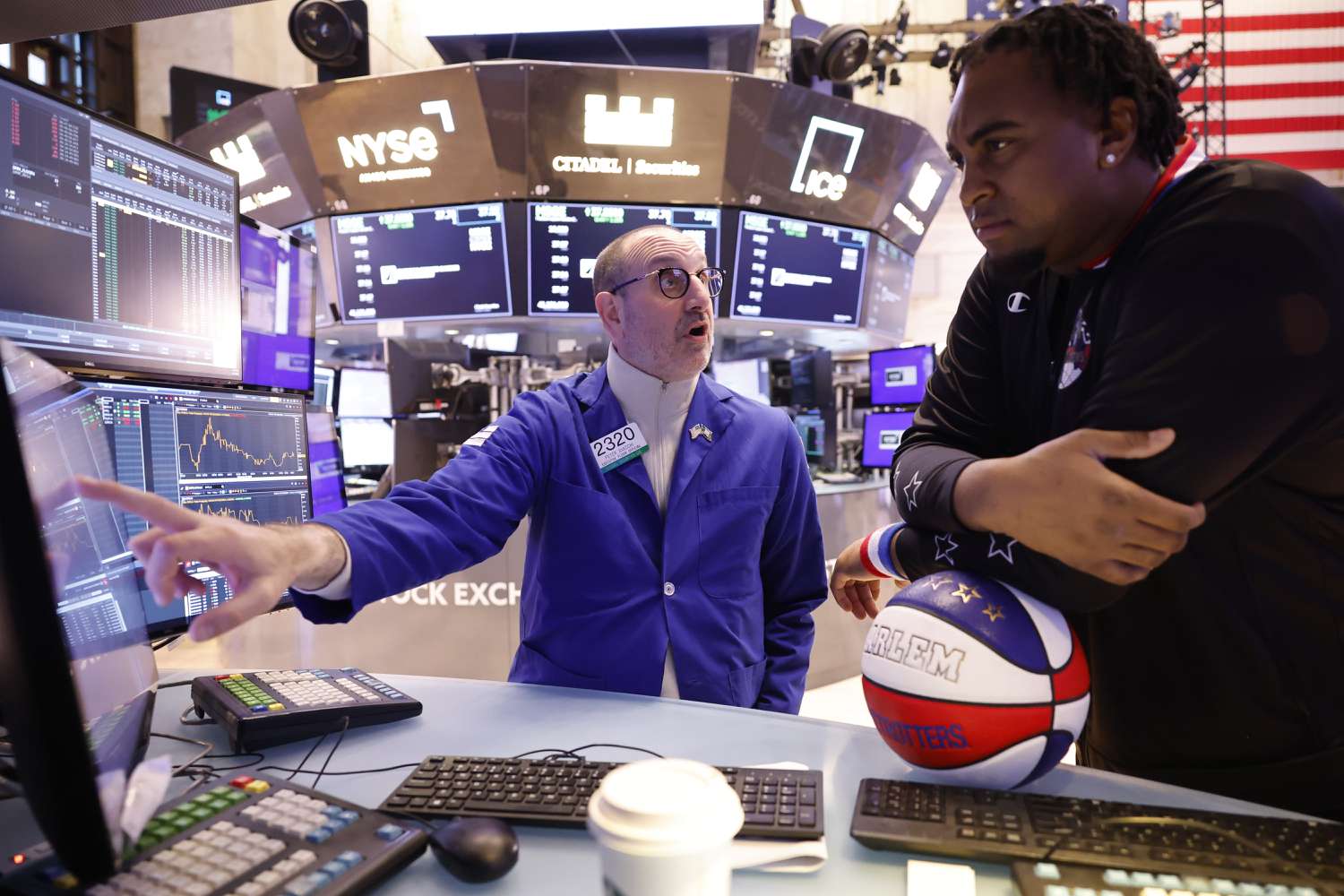 Trader on the floor of an exchange pointing to something on a monitor and explaining something to another person