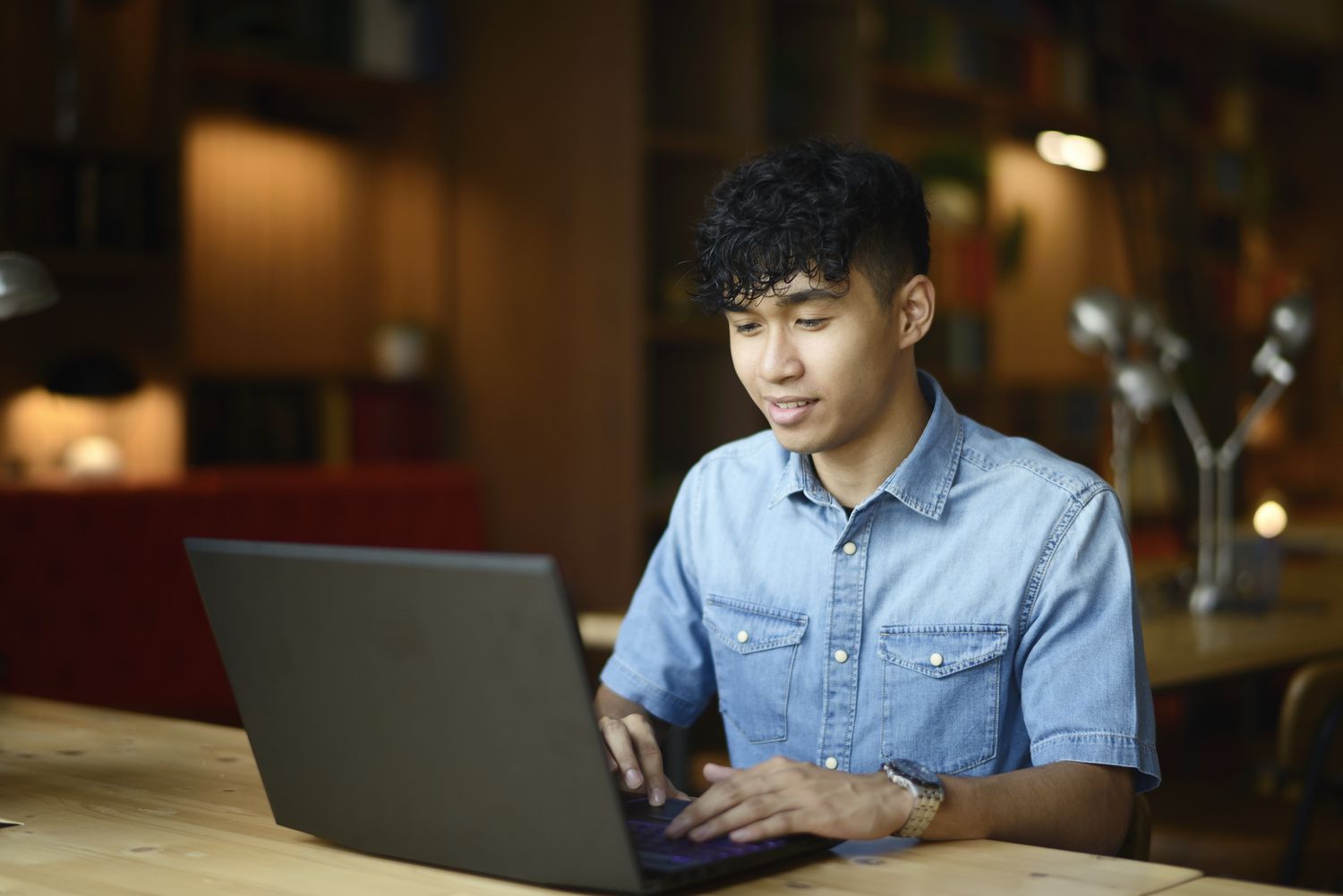 A man in a blue shirt sits at a table with a laptop