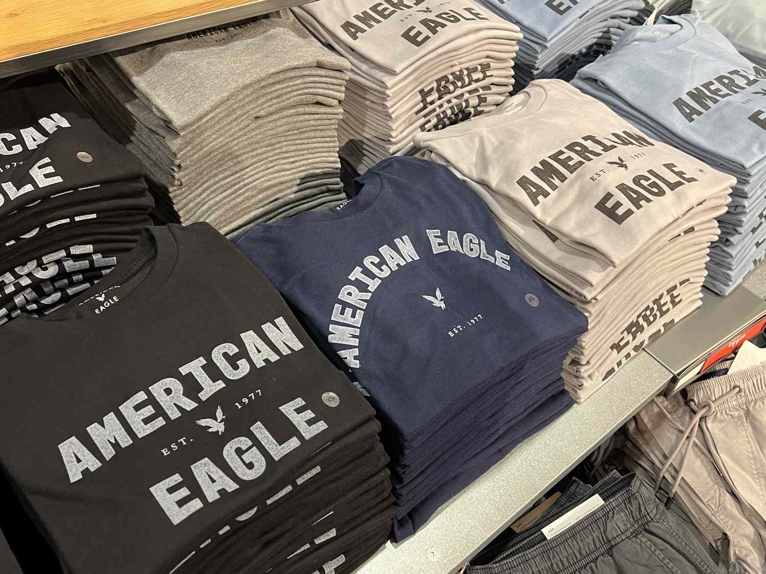 Stacks of American Eagle shirts sit on a display table in a store.