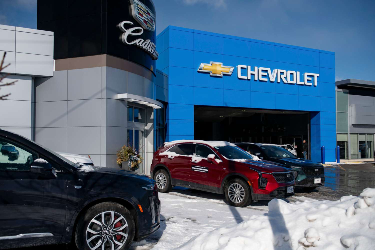 Cars are parked outside a Chevrolet and Cadillac car dealership with snow on the ground.