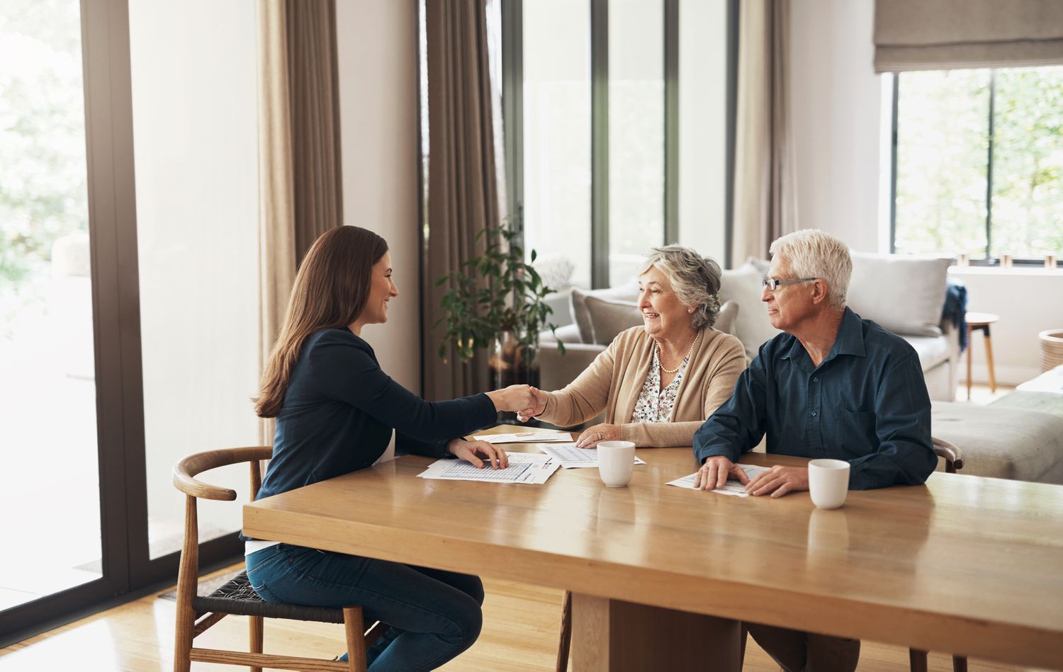 An elder law attorney shakes hands with her clients, a mature couple seated at a long table.