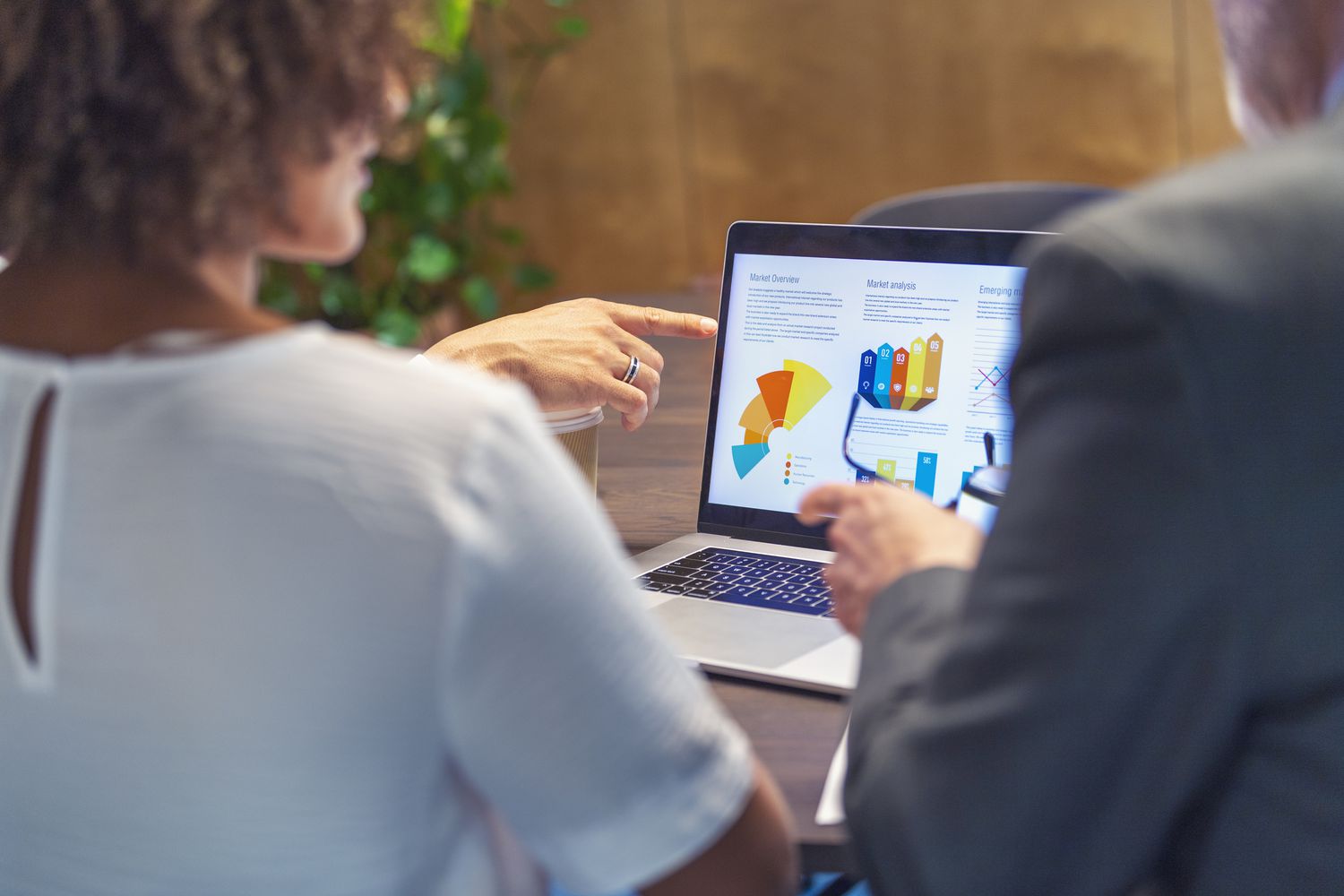 A financial advisor uses a laptop displaying color-coded portfolio allotment to explain investments to clients.