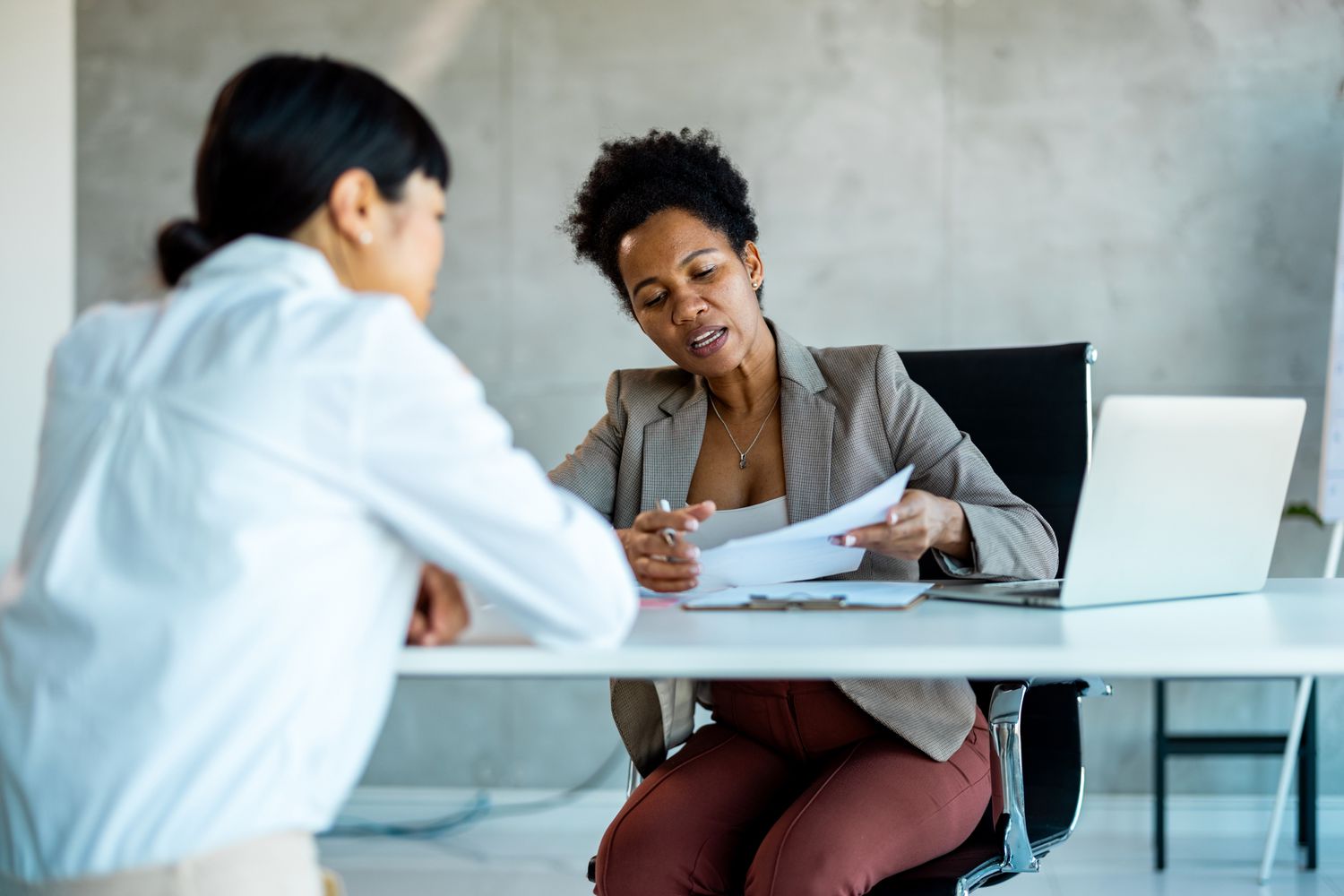 Two women sit at a desk reviewing a document with a laptop
