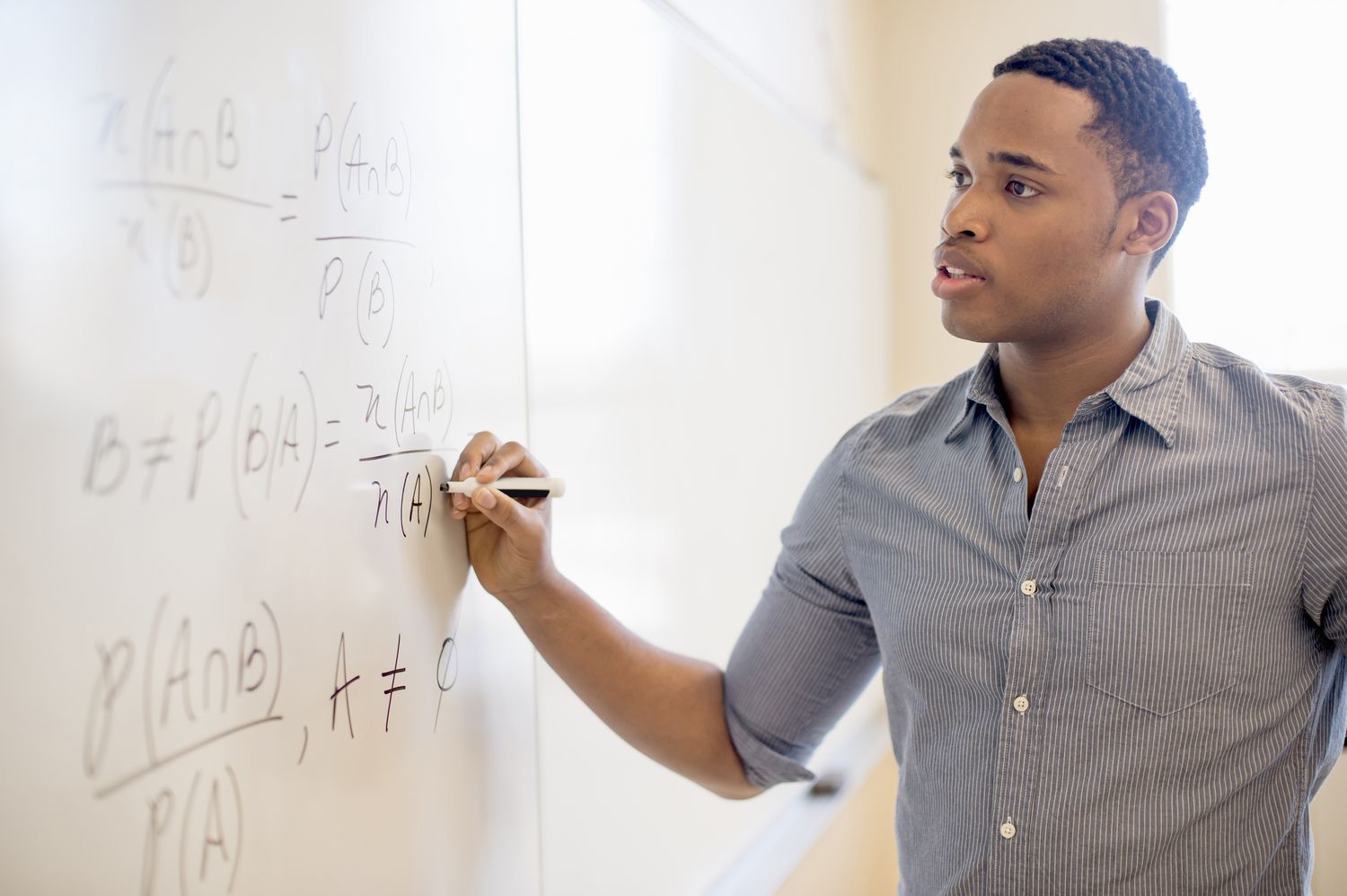 Student working out math equation on whiteboard in classroom
