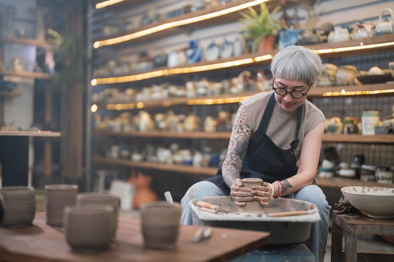 Senior woman artist making clay bowl on a pottery wheel in her studio.