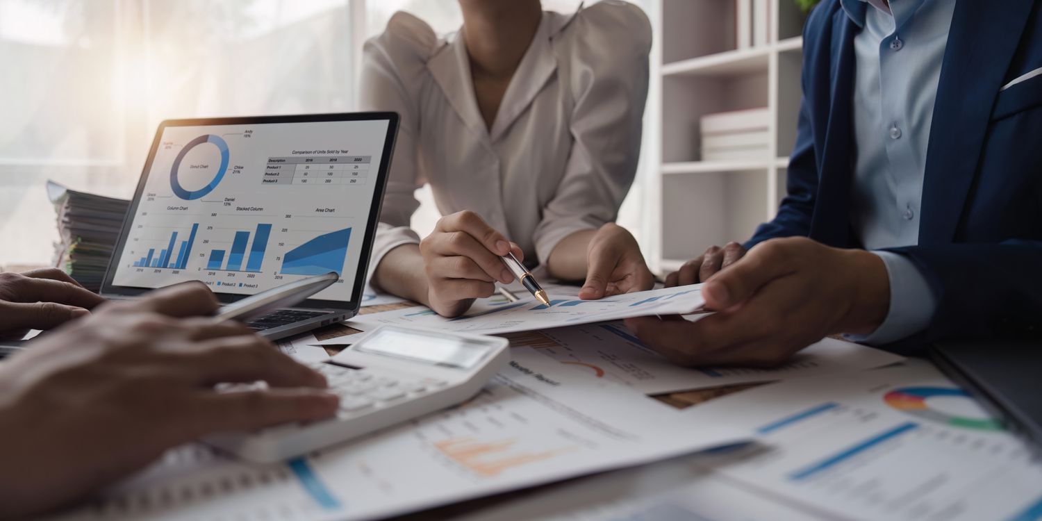 Three mutual fund managers gather around a table covered with financial reports to discuss the performance of various funds the company manages.