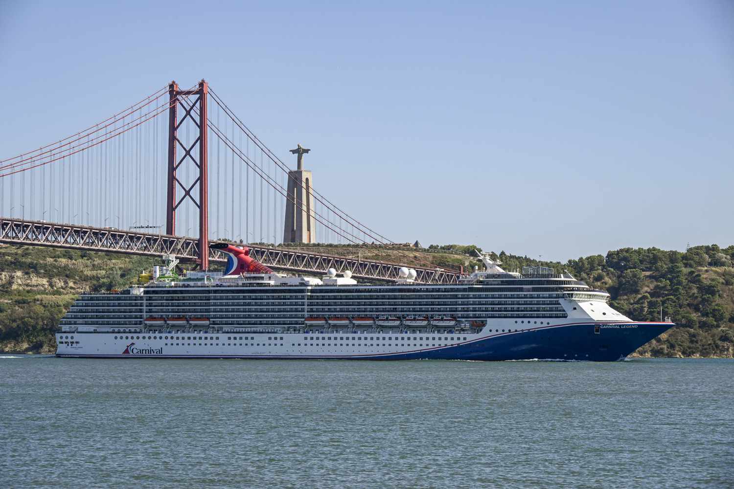  Carnival Legend, a 88,500 GT Spirit-class cruise ship operated by Carnival Cruise Line, sails past 25 de Abril Bridge on the Tagus River after leaving Lisbon cruise terminal on August 22, 2024, in Lisbon, Portugal. 