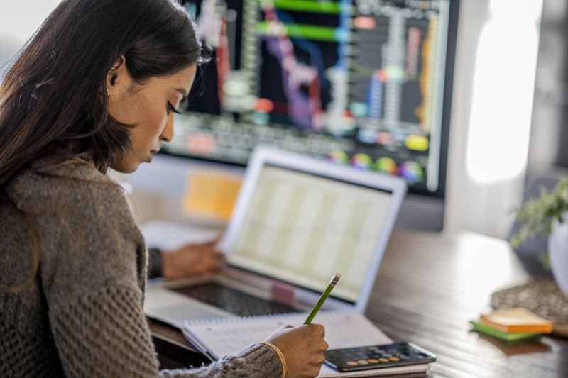 A person tracking stocks using a laptop and calculator.