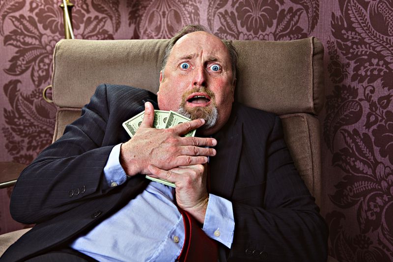 Middle aged man with a frightrened facial expression hugging US dollars
