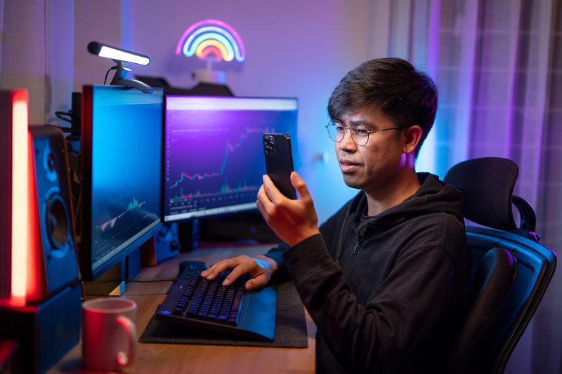 Young asian male trading and currency trading app on his smartphone 