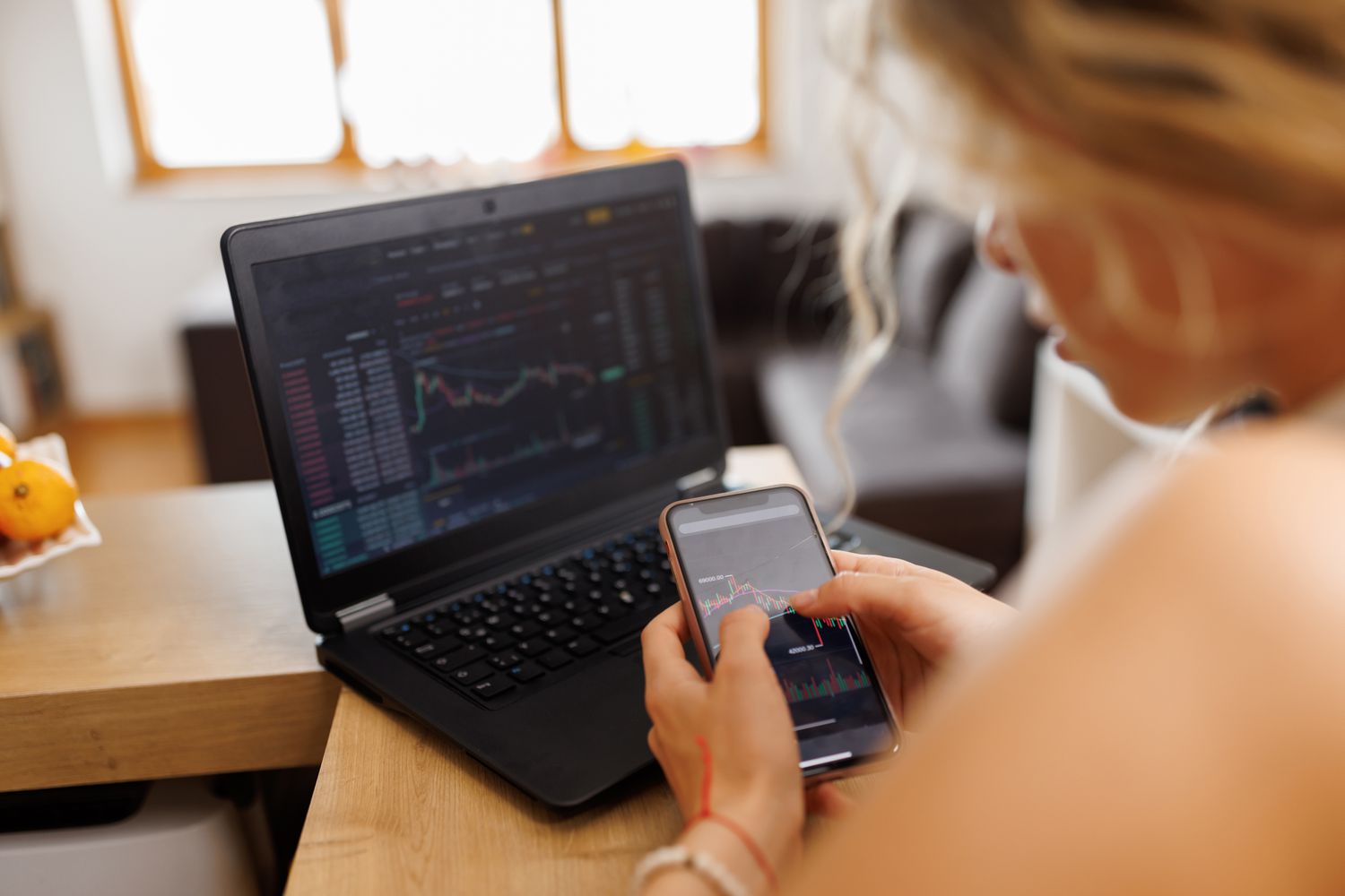 Woman sitting at a desk with an open laptop before her, while studying a chart on a smart phone.