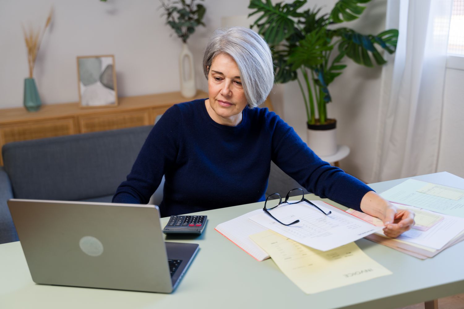 Woman in home office working on a laptop with a calculator beside it.