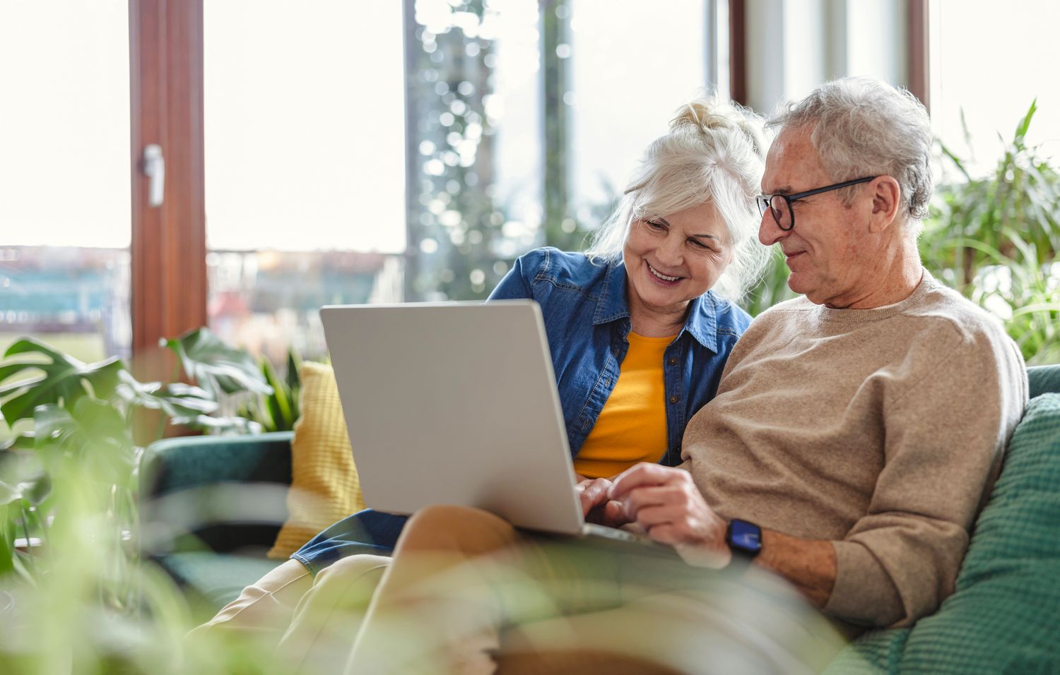 An older adult couple sitting together on sofa while looking at the laptop to read information about withdrawal benefits of their retirement plans.