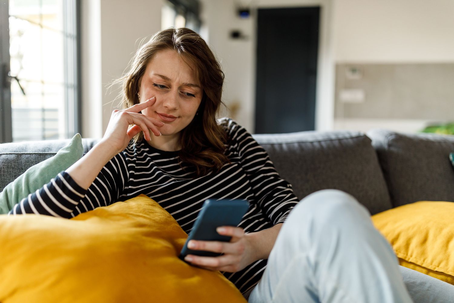 A woman sits on her couch looking at her smartphone