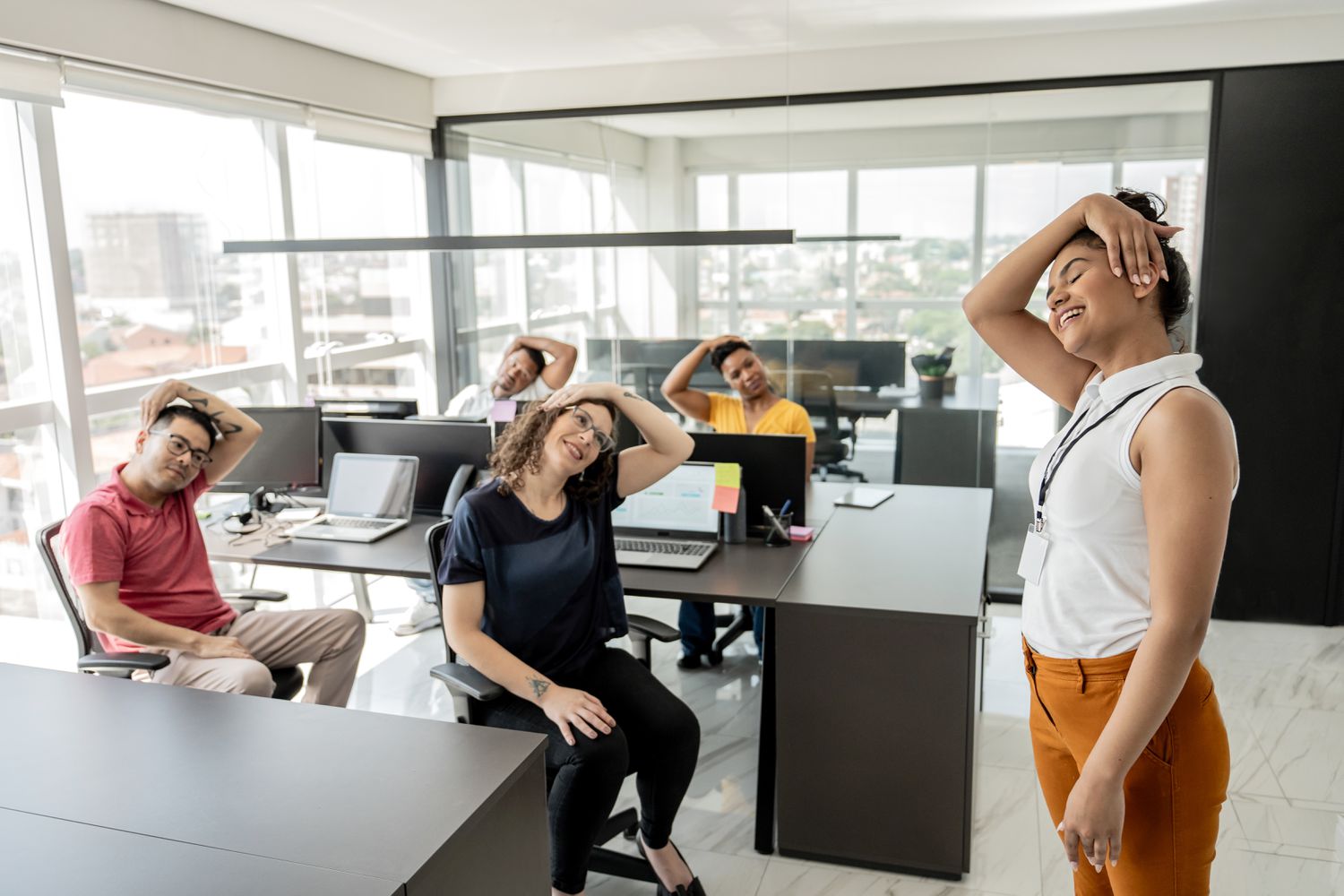 Workers do stretching exercises while sitting in office chairs at their workstations as part of the wellness program.