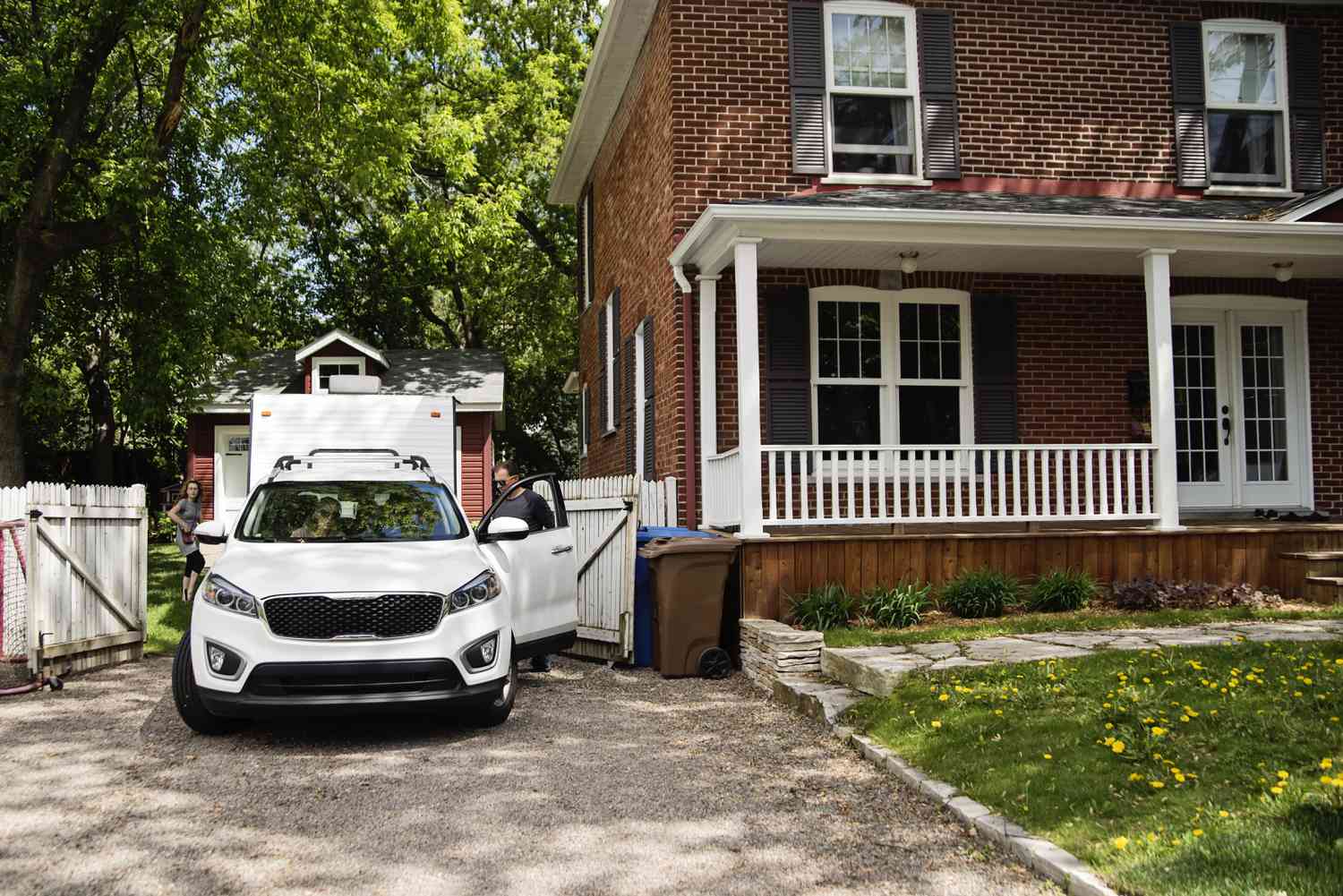 white car parked outside of a two story house with people in the car and others getting in