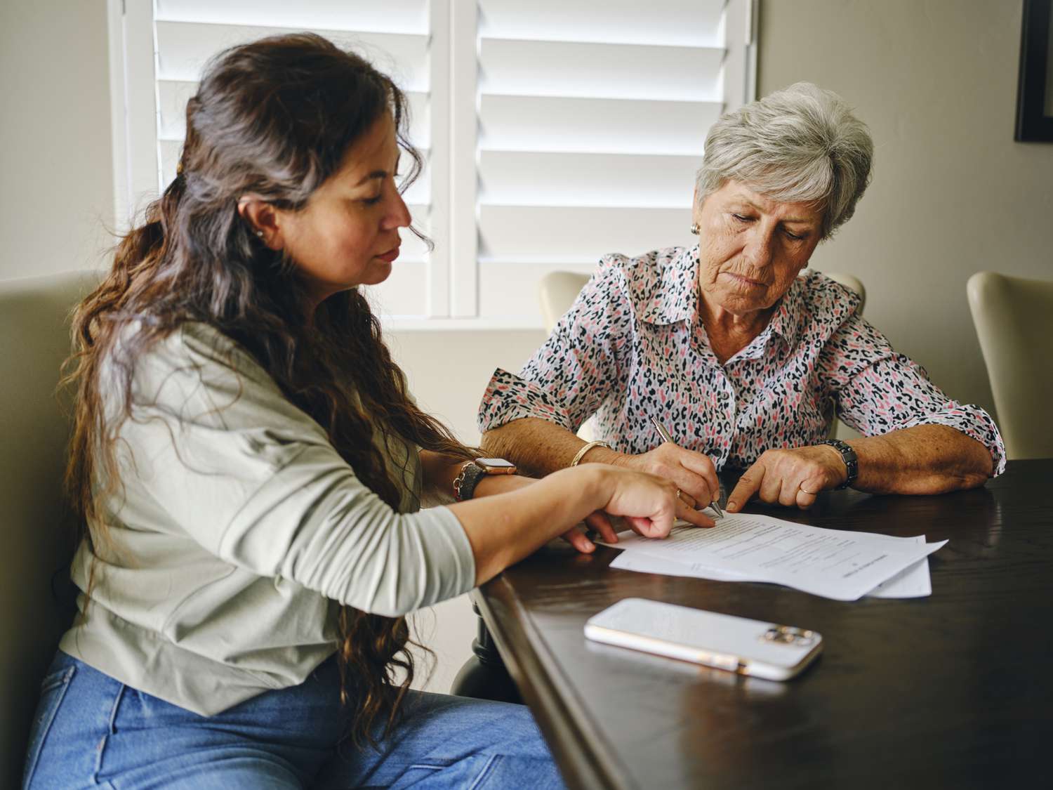 A senior woman signing paperwork with another person present.