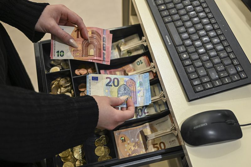 A worker holds euros at a cash register