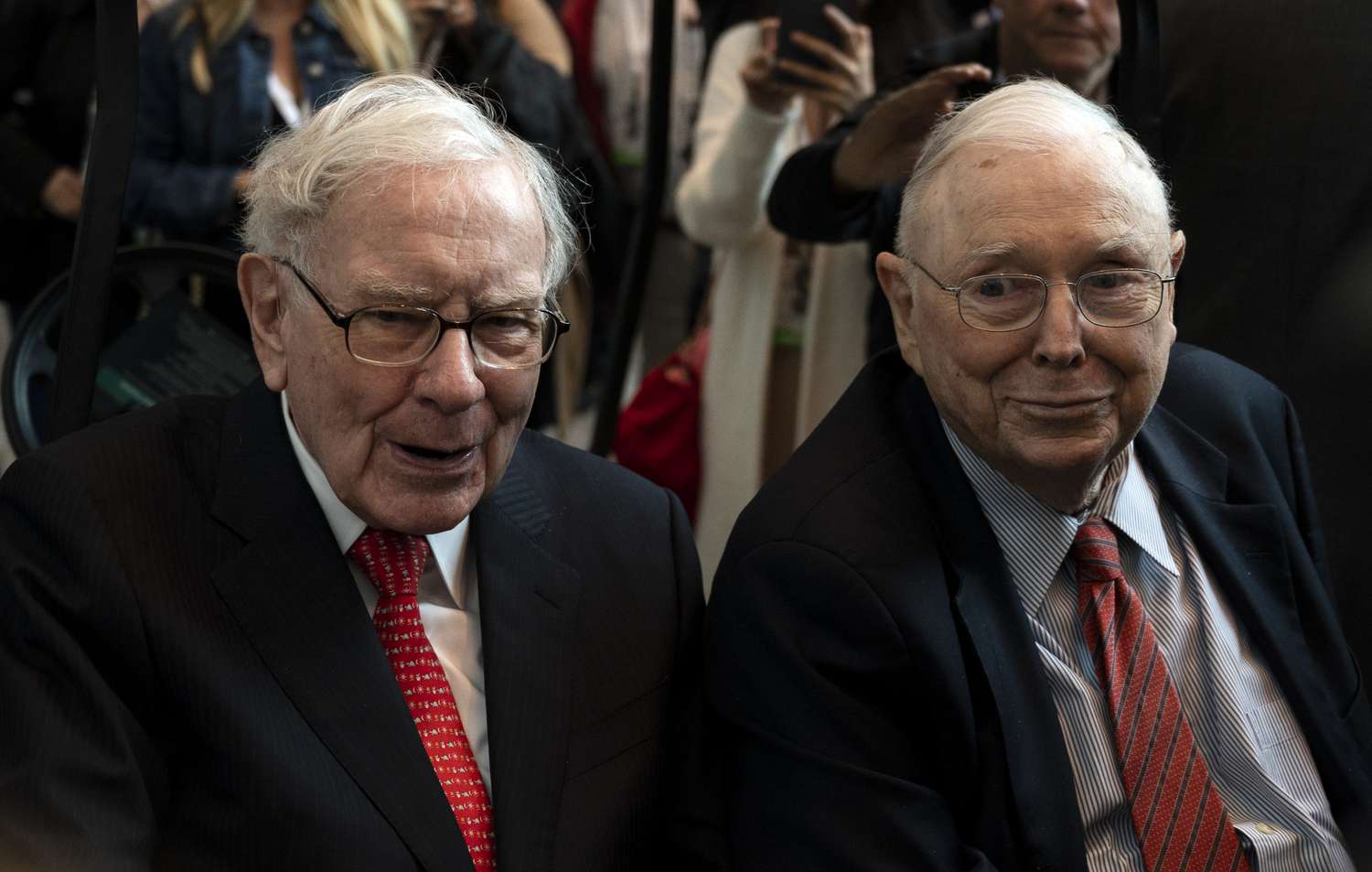 Warren Buffett and Charlie Munger seated together at an event, surrounded by people