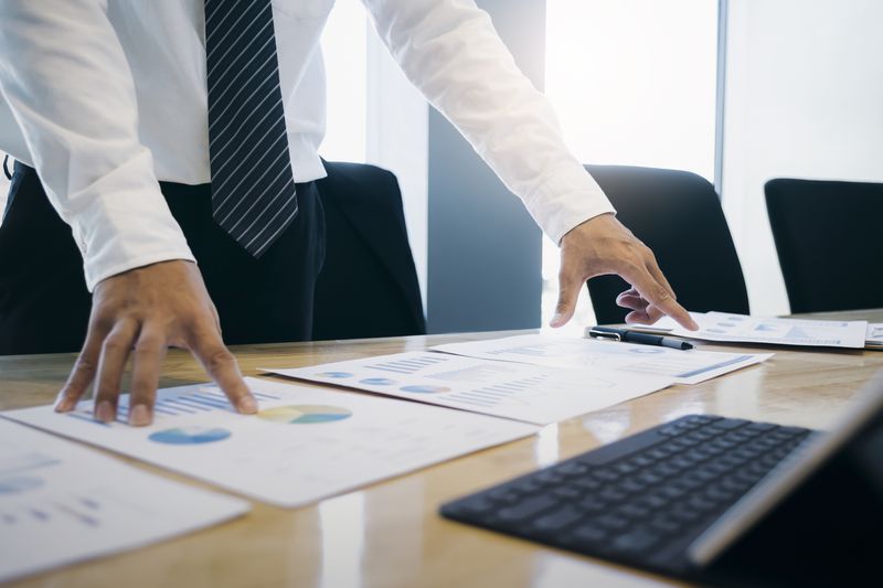 midsection of businessman analyzing papers on a conference table that contain graphs and charts and a laptop