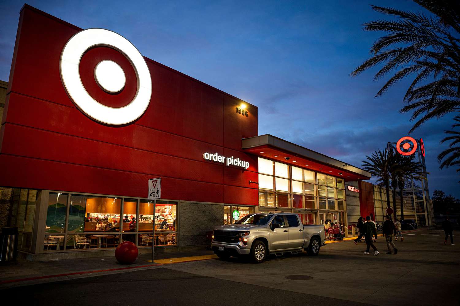 People and a silver truck are seen outside a Target store with a white Target logo on a red background, in front of a dark blue evening sky
