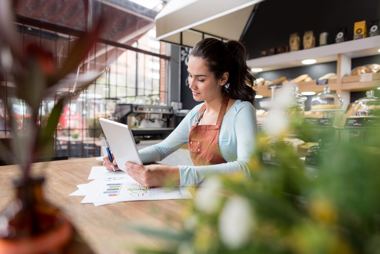 Woman working in a restaurant looking at a tablet and making notes.