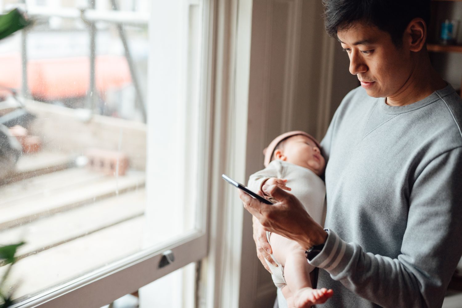 Young Asian dad holding infant and looking at phone