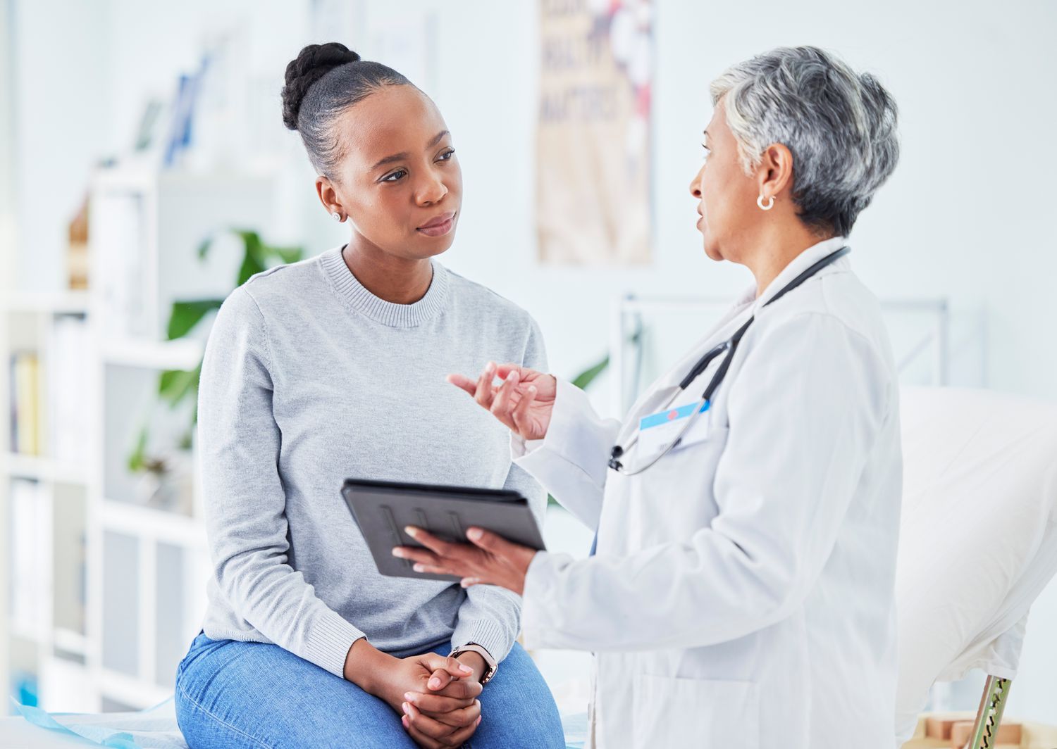 Female doctor talks to young woman patient while holding a tablet computer 