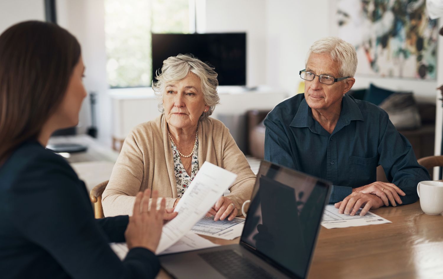 Woman talking to senior couple with paperwork in hand and a laptop in front of her. 