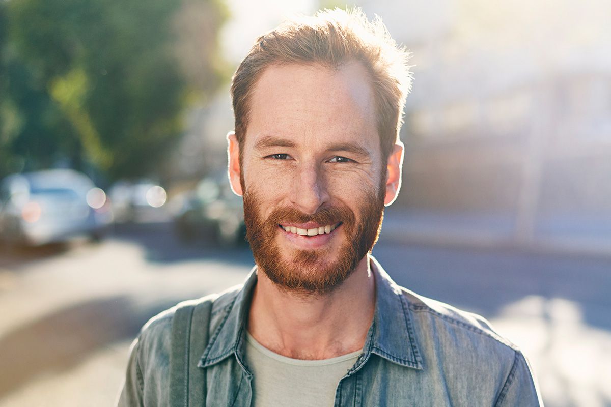 Man smiling with backpack and sun shining on him.