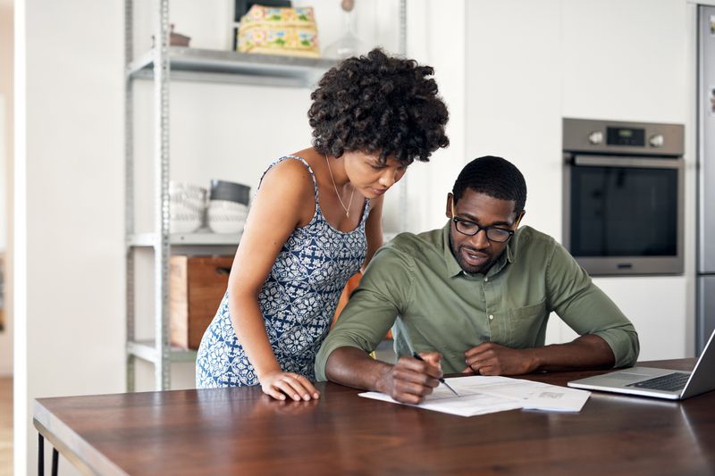 Two people looking through paperwork on a wooden table in their kitchen