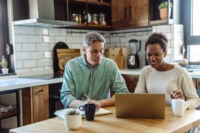 Couple in their 40s sitting at their kitchen table and looking together at mortgage rates on a laptop
