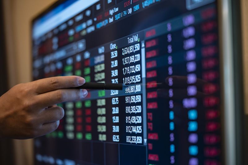 A person's hand pointing with a pen to options ticker information on a computer screen