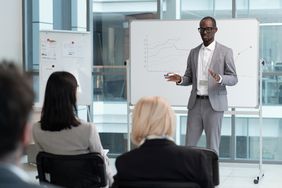 Person speaking to a meeting standing in front of a whiteboard with charts