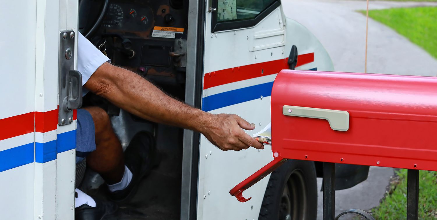 Mailman reaches out of his truck to deliver mail.