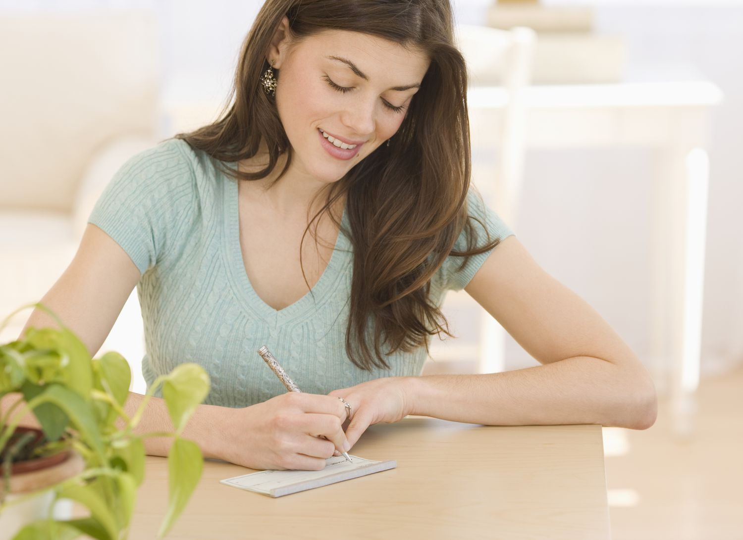 A smiling woman writes a check while sitting at a table.