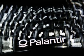 A blurred laptop keyboard and Palantir logo displayed on a phone screen. 