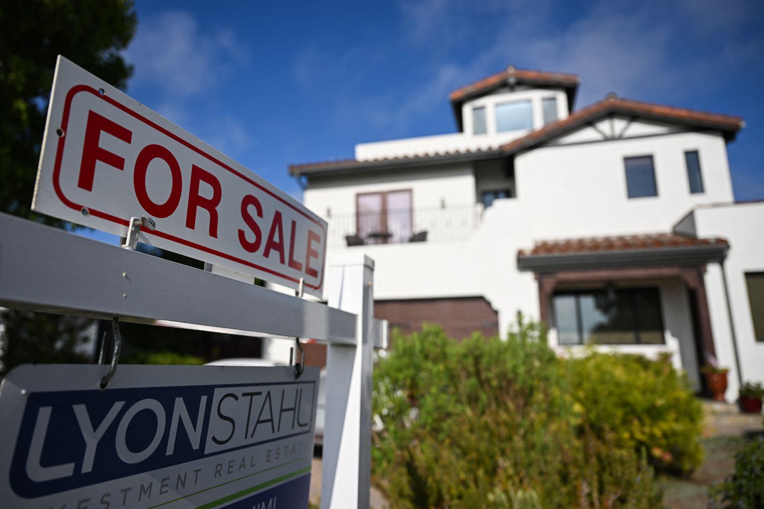 A for-sale sign is displayed near a white house. 